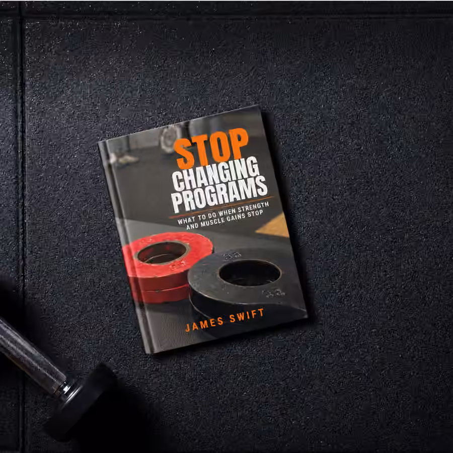 Stop Changing Programs book on a gym floor beside a dumbbell.